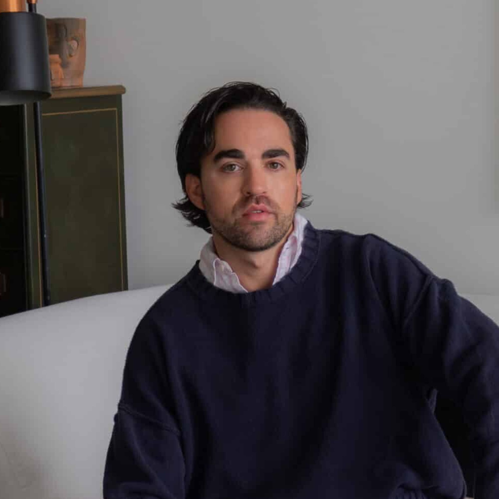 man with dark hair and navy jumper looking at camera