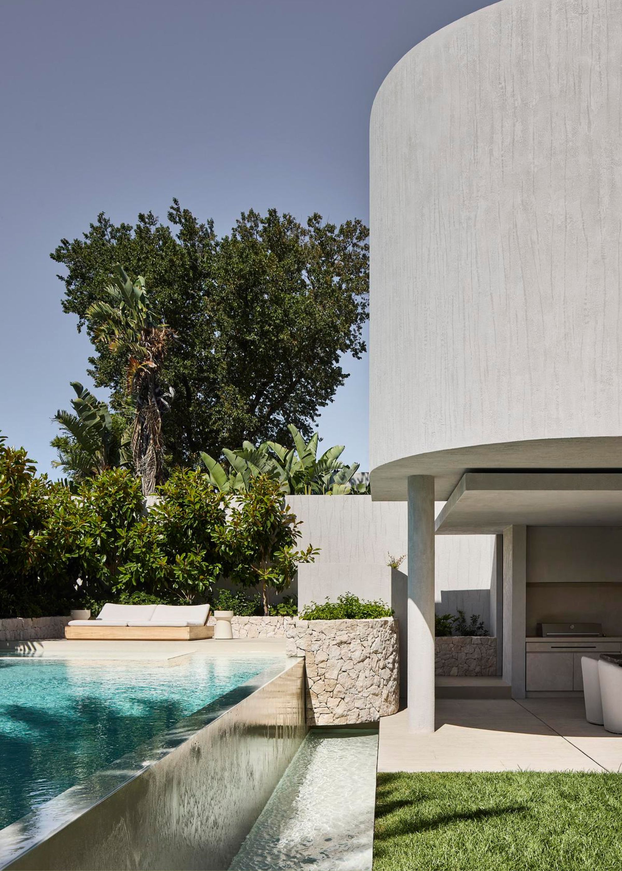 An outdoor pool with a sun lounger near some bushed and a tree