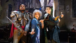 Three people in costume as fantasy adventurers with various props, with a city street background behind them