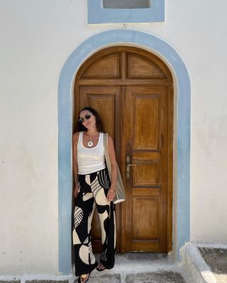 Anna LaPlaca wearing a white tank, printed pants, and flip flops with hardware