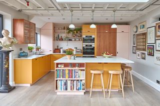 a pink and yellow ply kitchen with books on the island