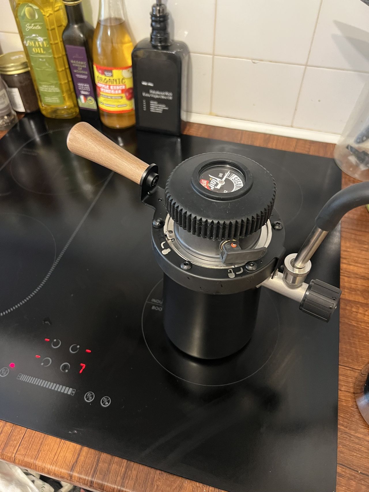 A black stovetop steamer with a wooden handle on a black hob on a wooden kitchen counter.