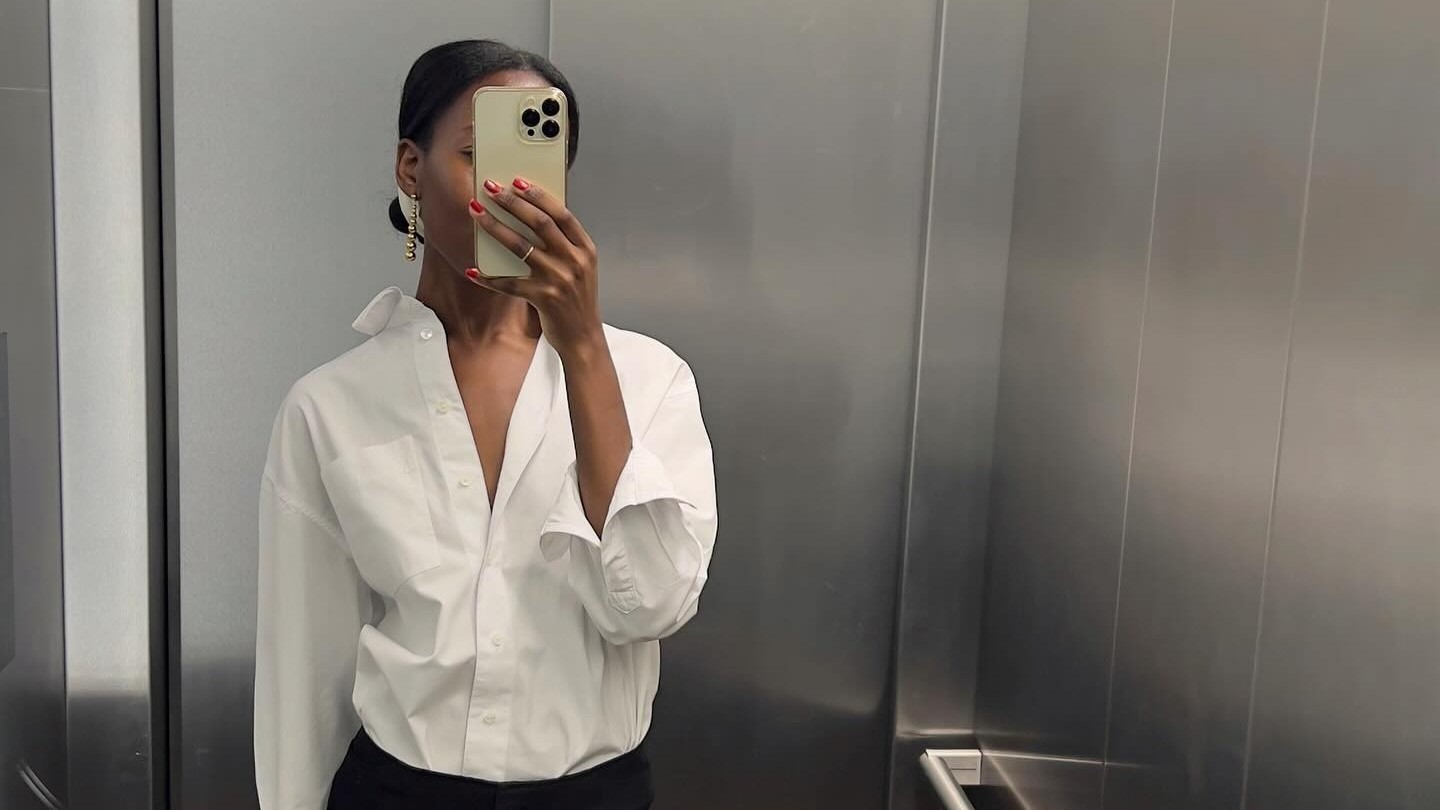 French woman wears black capri pants, white button down and black flat sandals in a mirror selfie. 