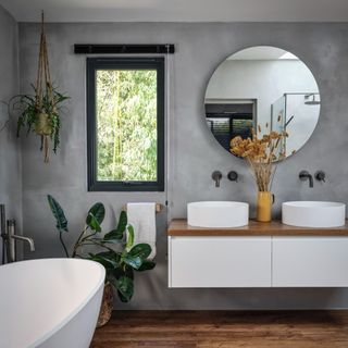 Bathroom with grey wall, bathtub, two basins and decorated with plants