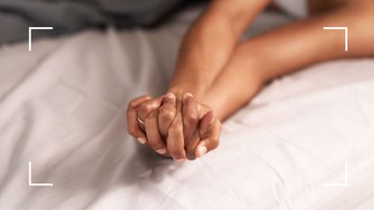 Image of two women's hands clasped together on a bed to represent transcendental sex