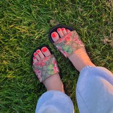 Photo of feet in black sandals with an orange-red pedicure on the grass