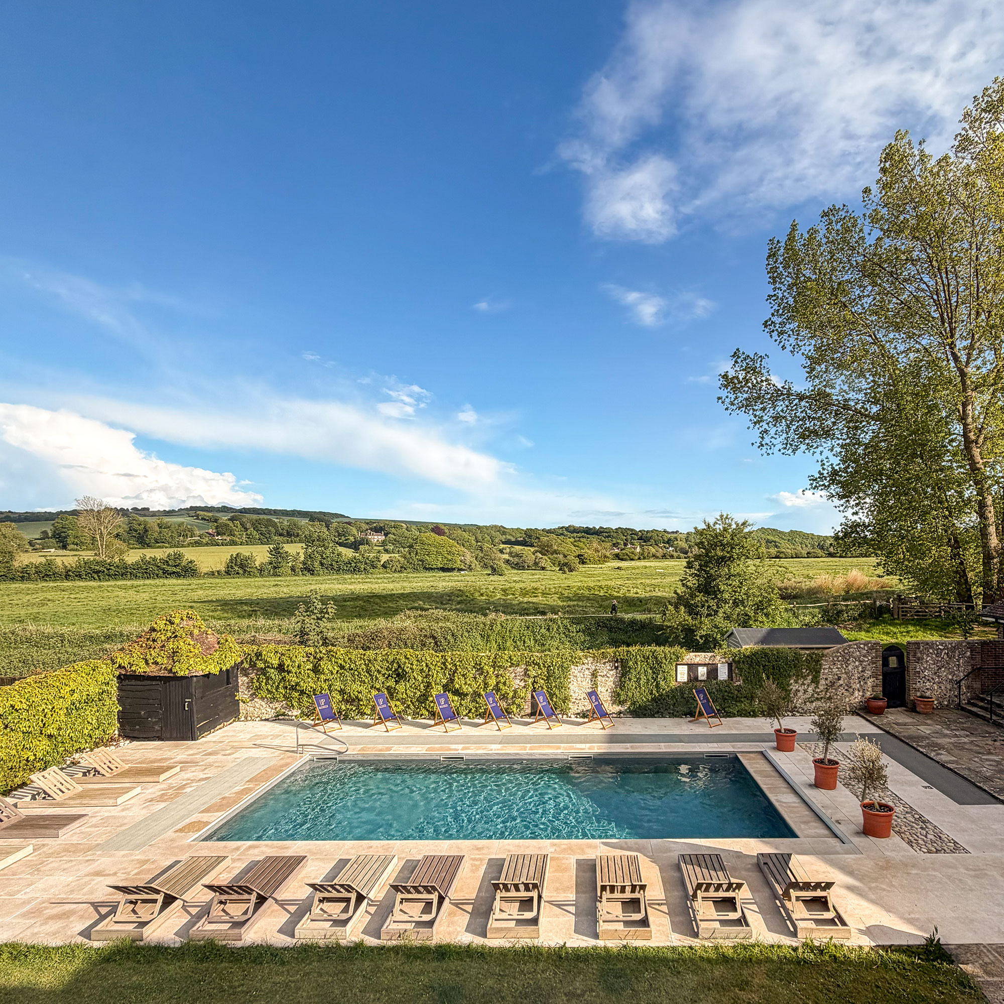 Outdoor swimming pool with row of wooden sun loungers surrounded by English countryside