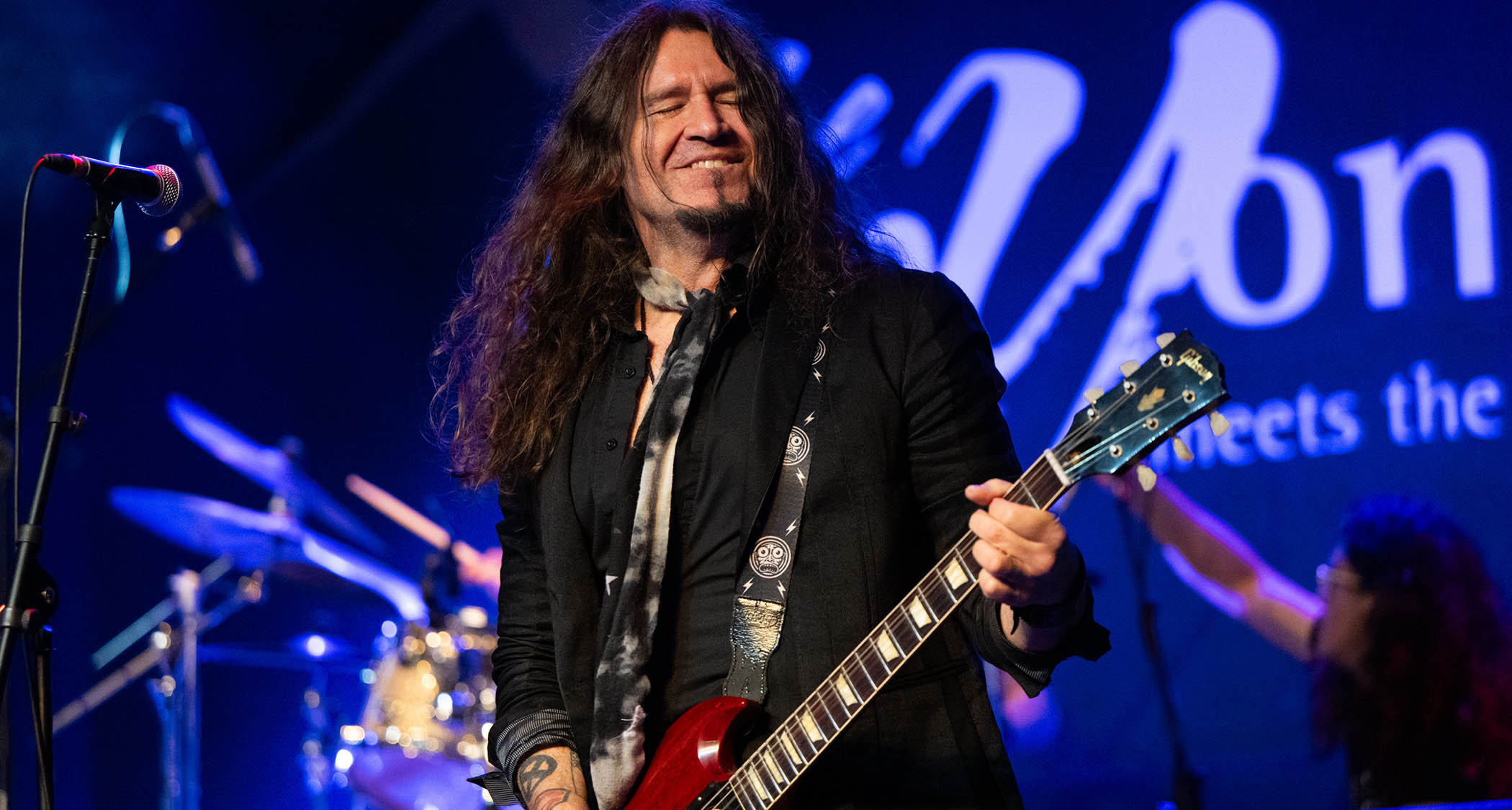 Phil X of Bon Jovi and the Drills smiles onstage as he plays a cherry red Gibson SG.