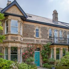 exterior of an Edwardian house with double bay windows, teal front door with roses around it and balcony