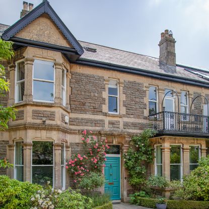 exterior of an Edwardian house with double bay windows, teal front door with roses around it and balcony