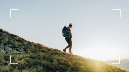 Woman doing walking as a workout down a hill with backpack and hiking gear on, sun poking out behind the grassy hill