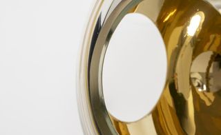Detail of the convex vase made of silver mirrored surface outside, with a round opening showing the golden surface inside.