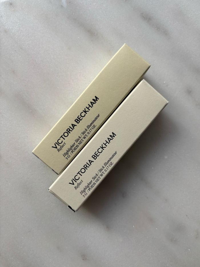 The Victoria Beckham Reflect Highlighter Stick in its packaging on a marble table