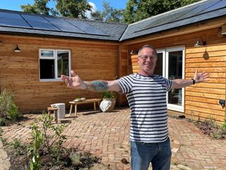 Mark Millar stood in front of newly built timber frame house with solar panels.