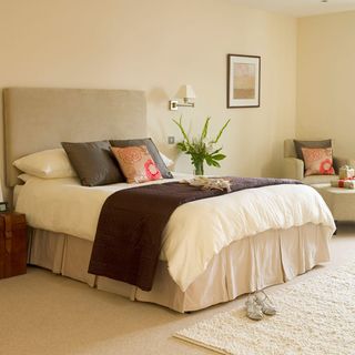 bedroom with cream colour wall and flooring bed with designed cushion and sofa chair