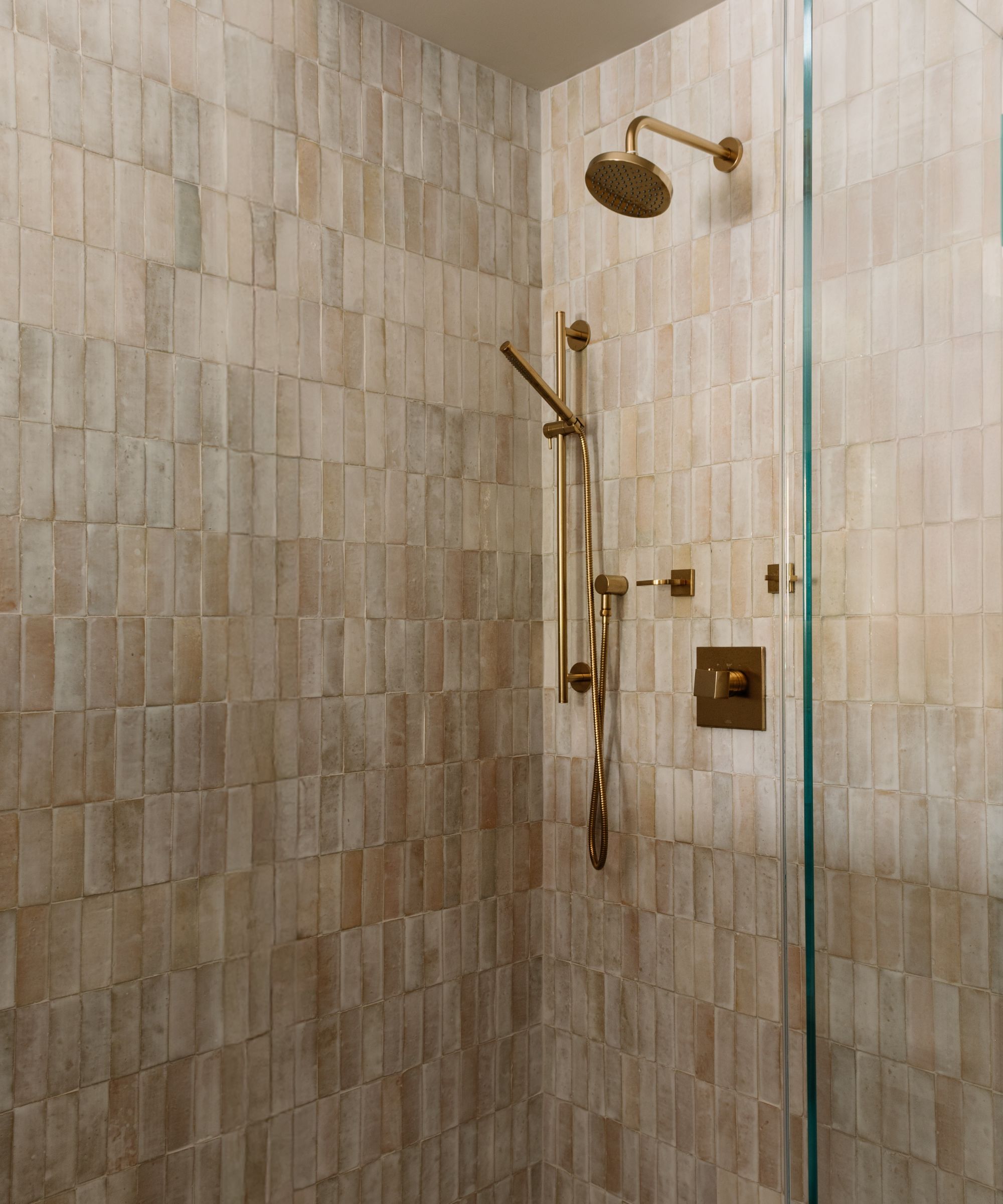 Walk in shower with gold hardware and beige textured tiles