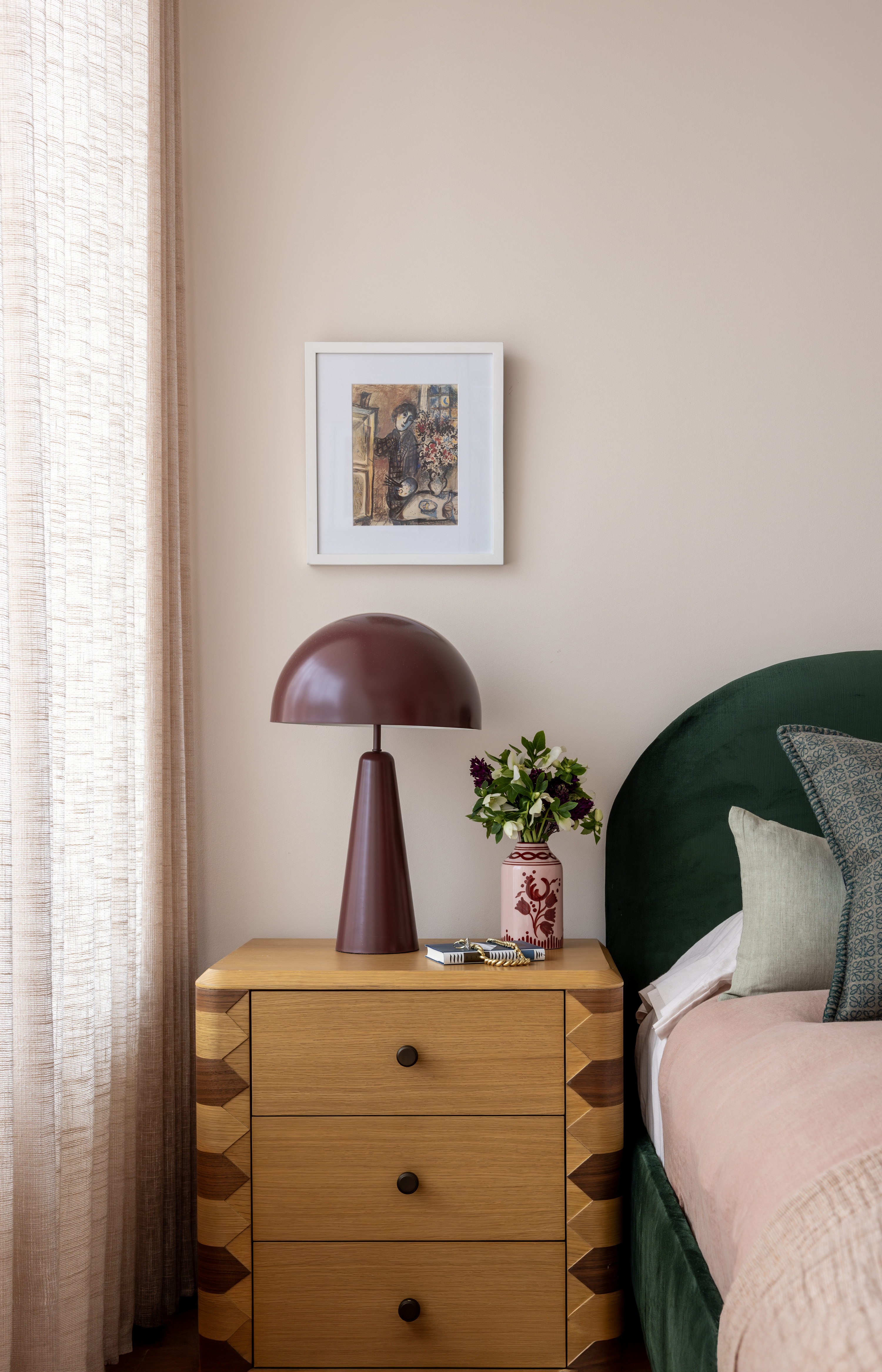 A bedroom with pink bedding, green headboard and a wooden side table