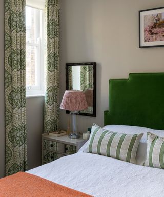 smaller bedroom with green headboard, patterned curtains, orange throw on bed, small mirror behind bedside light