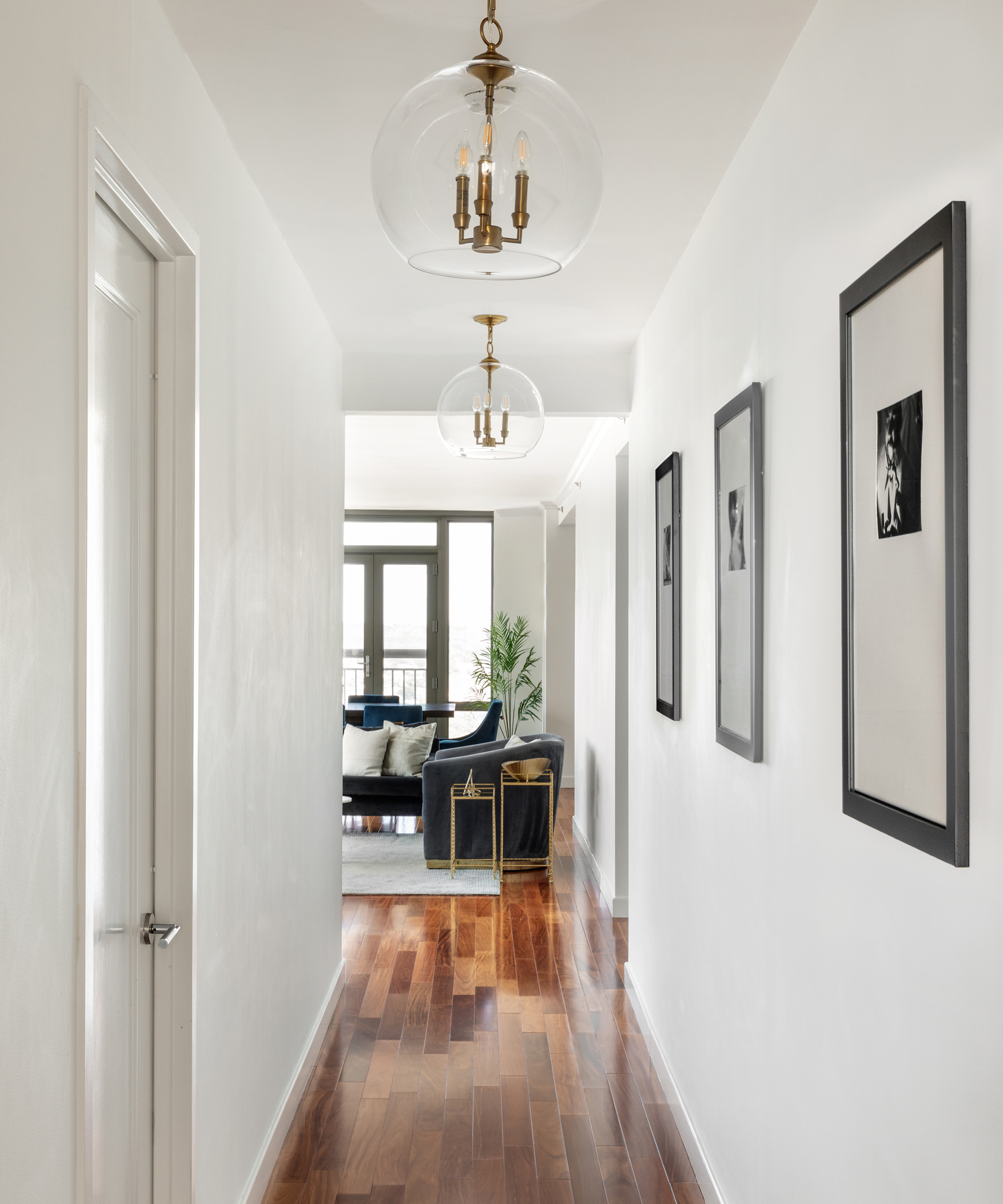 White narrow hallway with glass sphere ceiling pendants, and trio of black framed photo art.