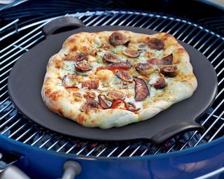 The Emile Henry glazed pizza stone by Crate & Barrell sitting on top of a bbq grill grate