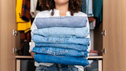 TikTok jeans hack could help you find the right size, here a woman stands in front of a wardrobe holding stack of blue jeans