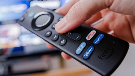 Person holding an Amazon Fire Stick with a TV in the background