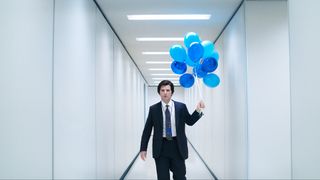 Adam Scott&#039;s Mark Scout in Severance season 2 holding blue balloons as he walks down an ominous hallway