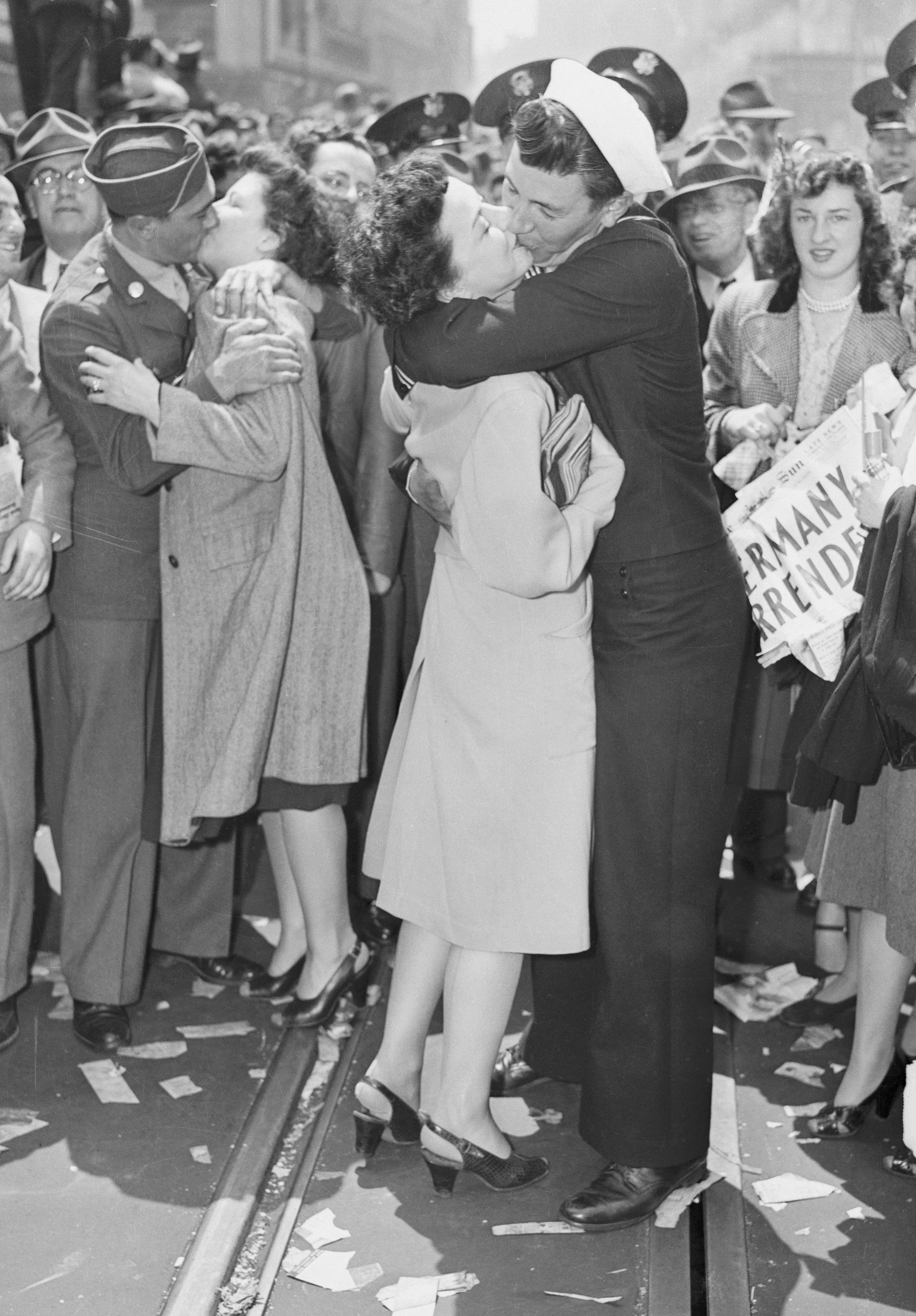 While watched by a celebrating crowd, women get kissed by US military men at Times Square on V-E Day, May 7, 1945