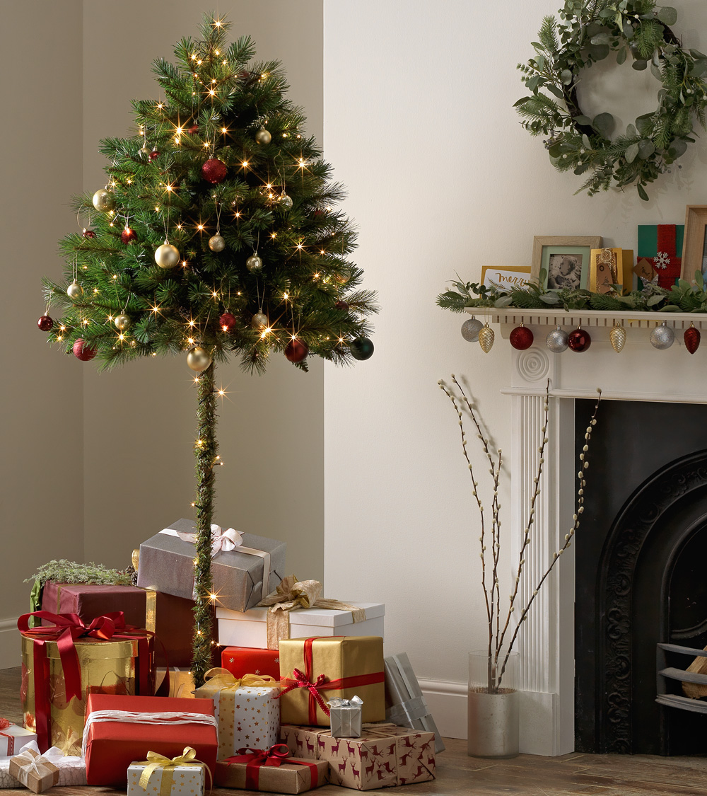 Half parasol Christmas tree decorated with lights and surrounded by gifts in a cosy living room.