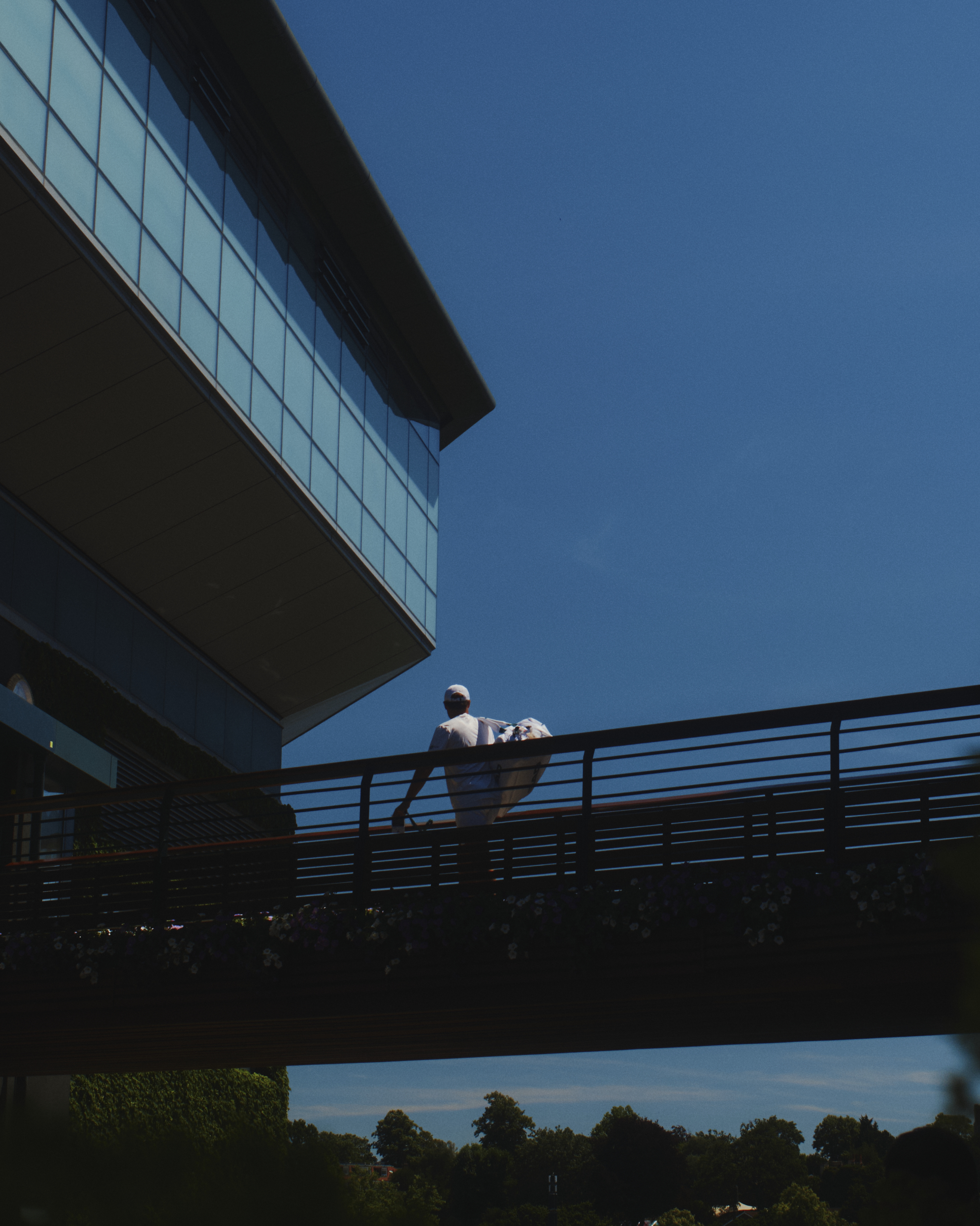 Tennis player crosses walkway at Wimbledon, backdropped by blue sky