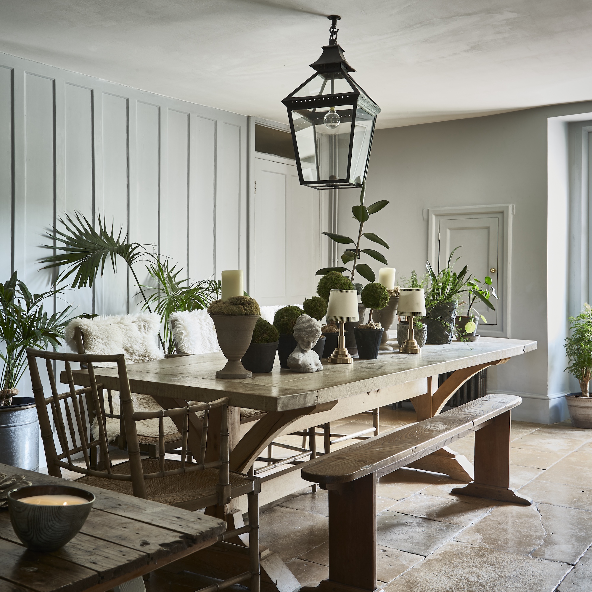 dining room with rectangular wooden table with chairs and bench seat, with wireless lamps and stone heads and vessels on table surface