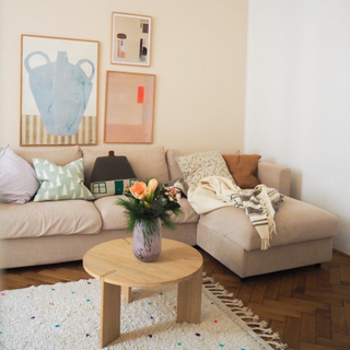 Happy, playful lounge nook with abstract, pastel wall art, chaise sofa with assorted, patterned scatter cushions, and small round wooden coffee table with vase of fresh flowers.