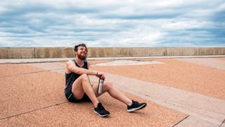 Sweaty man in running clothes sits on ground smiling