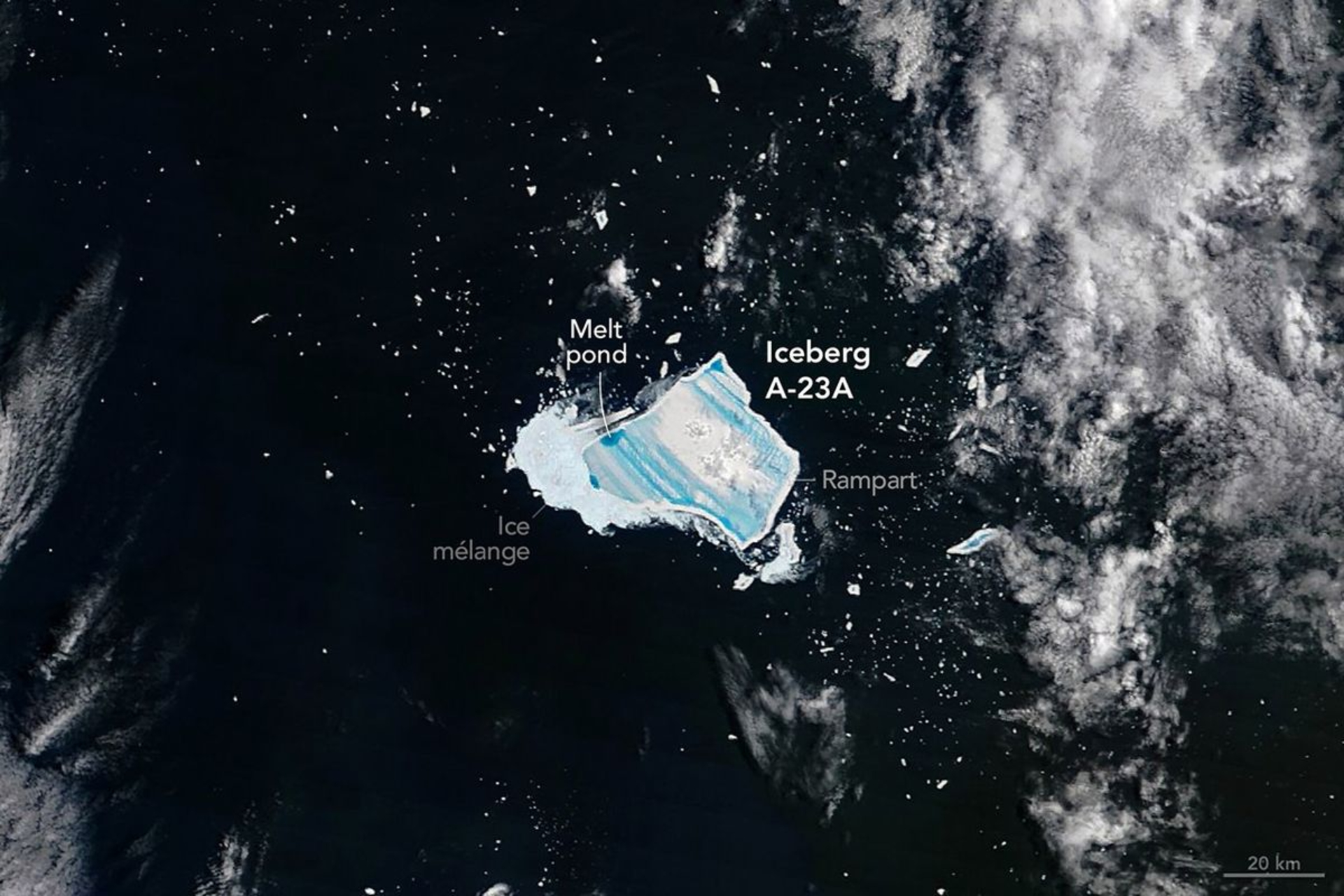 A blue jagged shape is seen in dark waters with white foam from the sea with the large white label Iceberg A-23A next to the blue shape