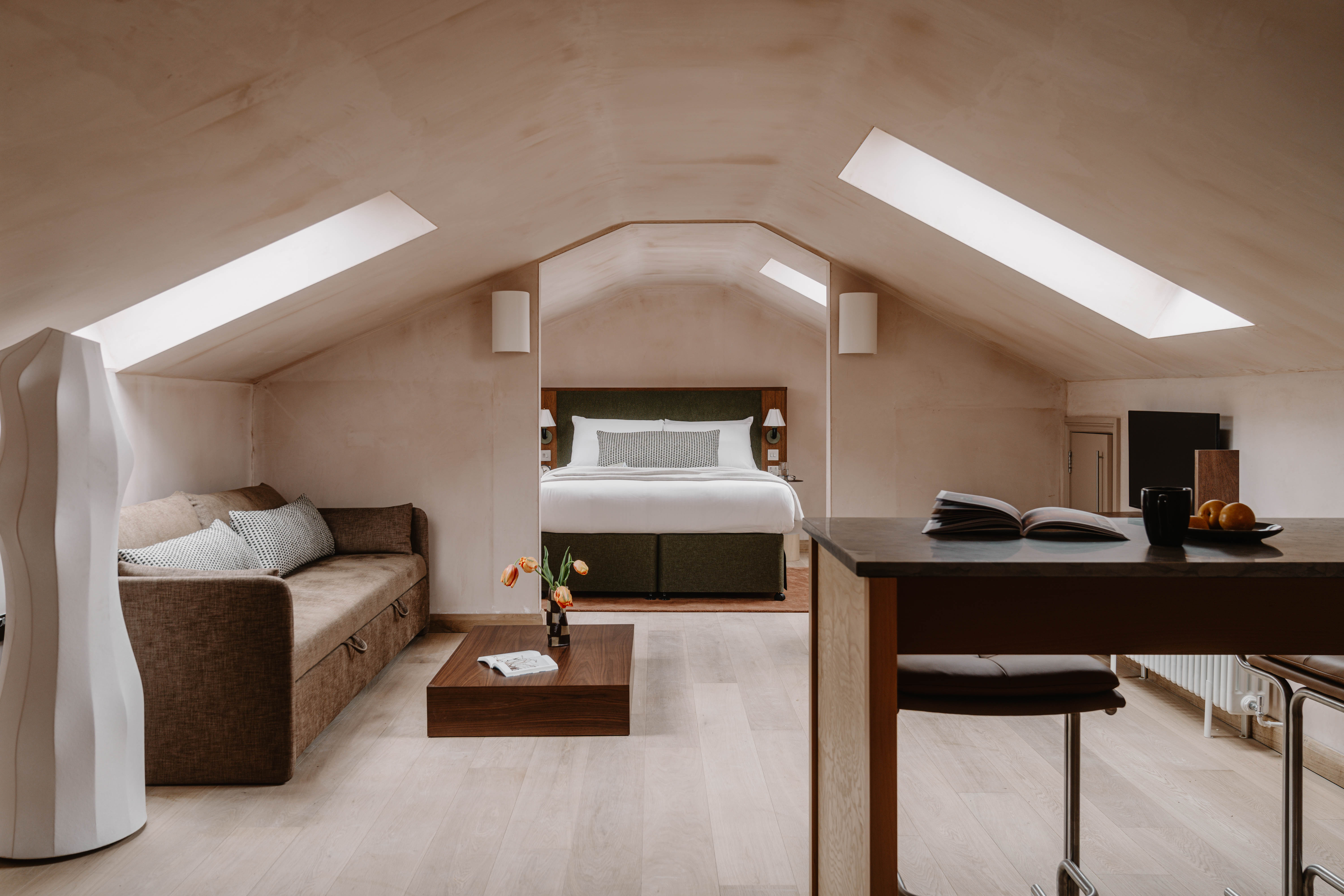A neutrally tinted hotel with argilla-toned walls, sculptural furnishings, wooden surfaces, and curated art and tilework.