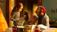 A stop-motion still showing a teenage girl holding a cracker box, a toddler and a bearded man in a red beanie gathered around a kitchen table lit by warm lamplight.