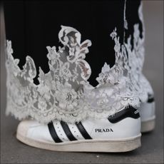 A woman at fashion week wears a pair of prada sneakers with a lace skirt