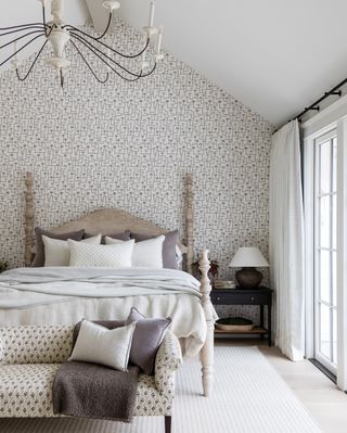 white bedroom with washed wooden bed, patterned wallpaper and bench and chandelier