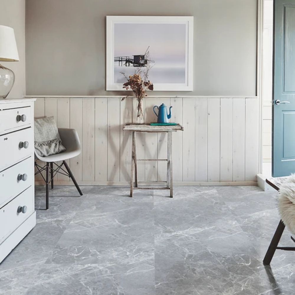 A bedroom with large-scale grey marble effect floor tiles and whitewashed furniture