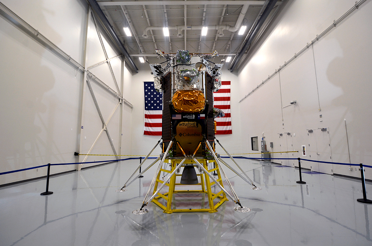 a rectangular spacecraft sits behind a barrier in a white cleanroom