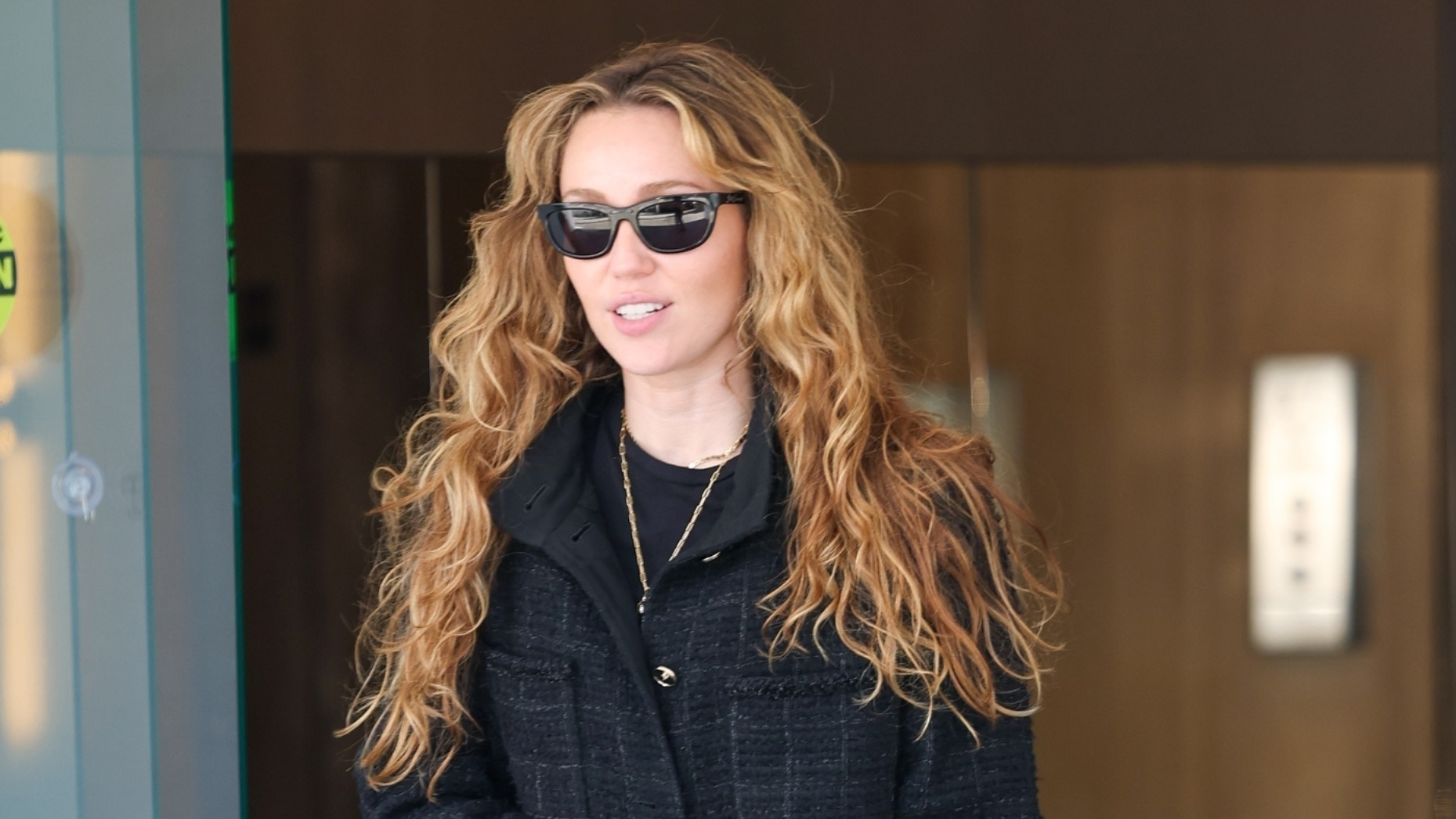 Miley Cyrus wearing a black tweed jacket, straight-leg jeans, and lug-sole boots