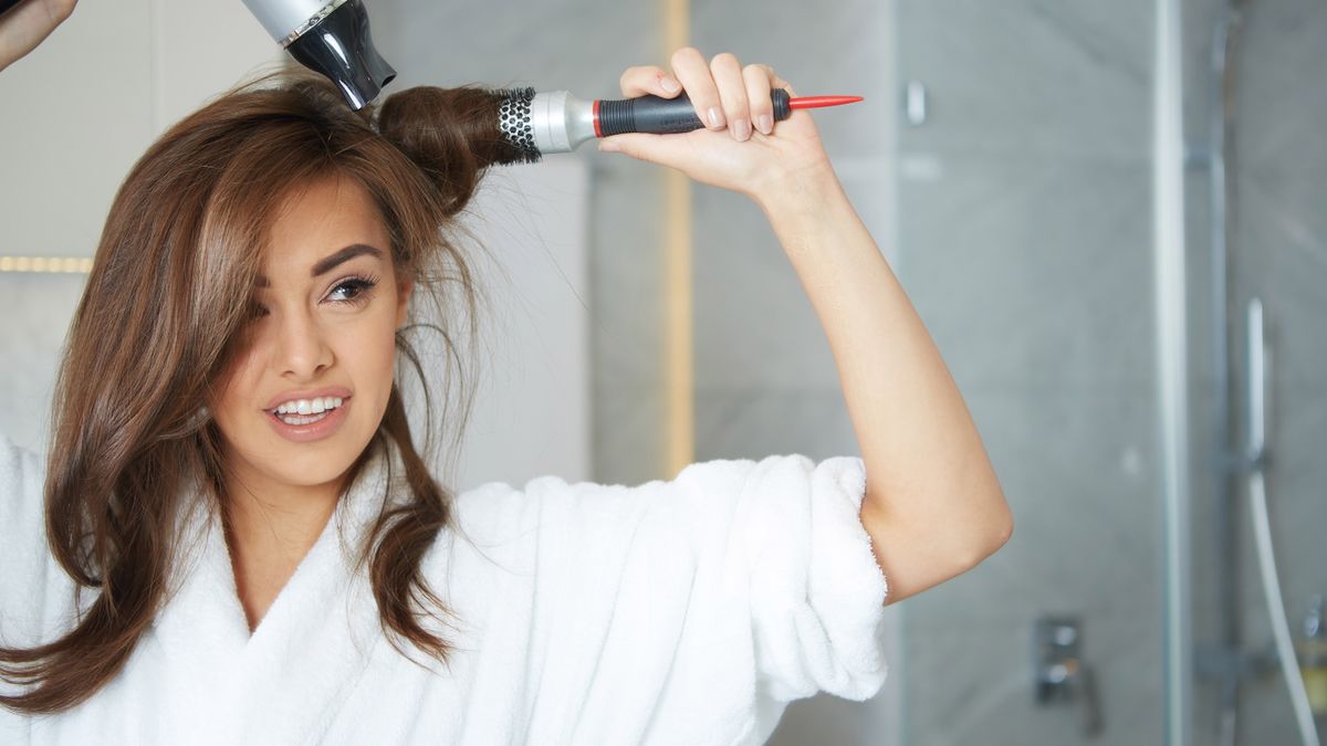 A woman blow drying her hair with a hair dryer and barrel brush