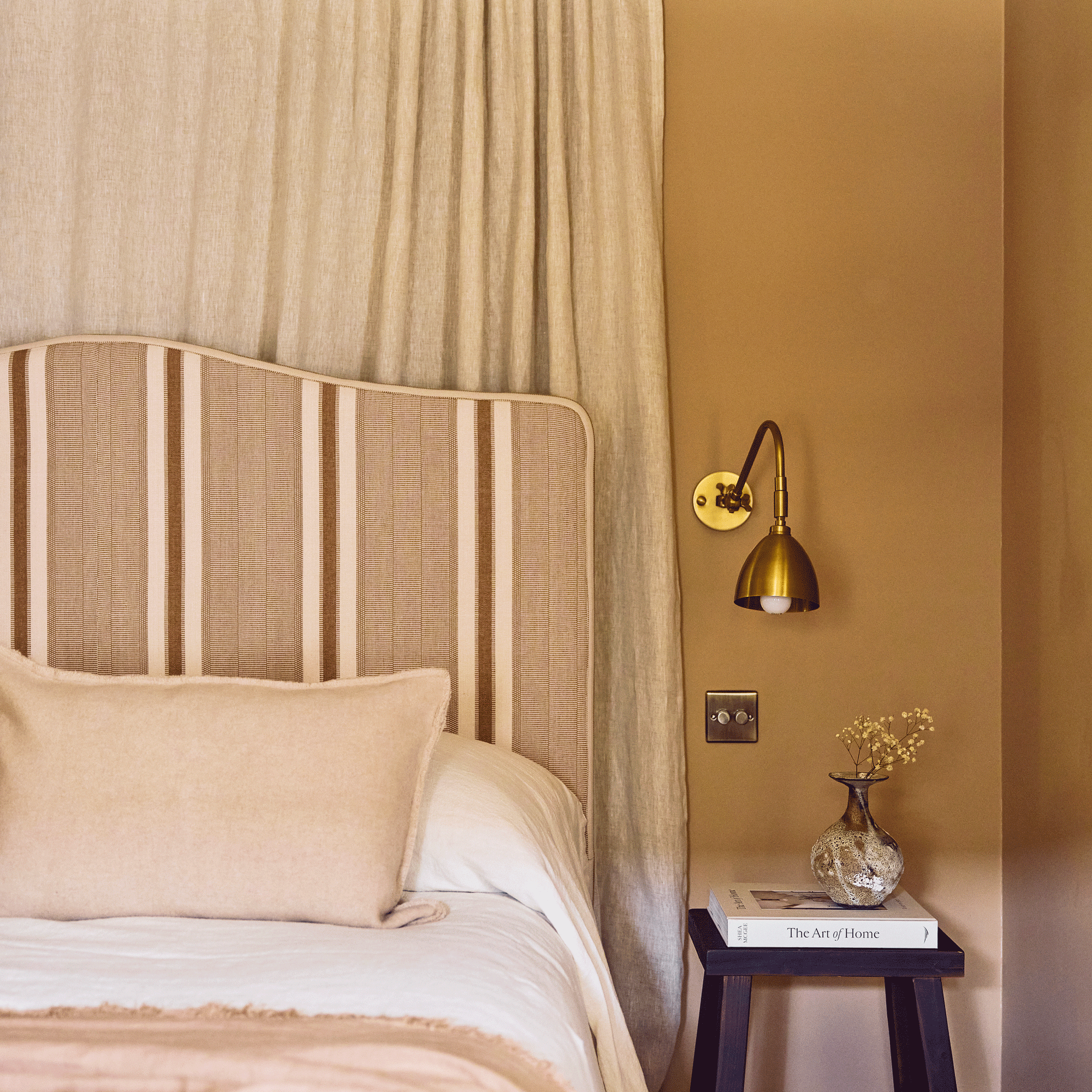 a bedroom with yellow walls, a striped headboard and a wall-hung curtain behind it