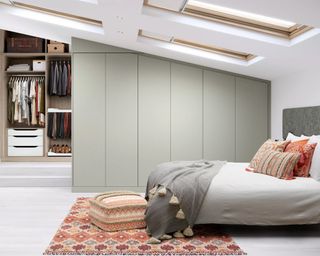 A loft bedroom with fitted sage green wardrobes and skylight windows