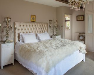 neutral cottage bedroom with silk headboard, faux fur throw and gilt lights