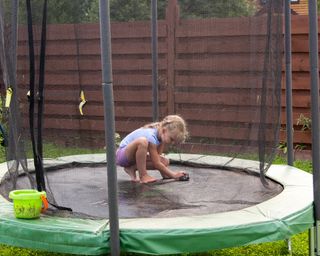 little girl washes her trampoline in the backyard