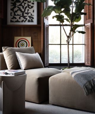 dark wooden panelled room with a large window with shutters and a soft velvet chair and footstool designed for a reading corner