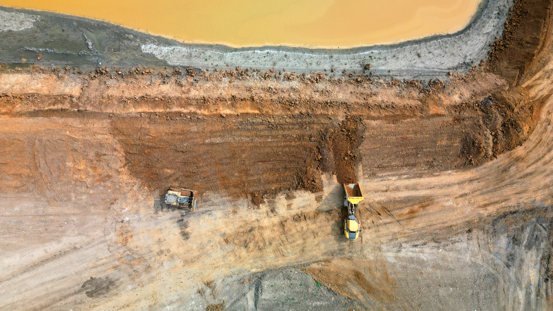 An aerial view of two bulldozers moving waste around in a vast landfill site.