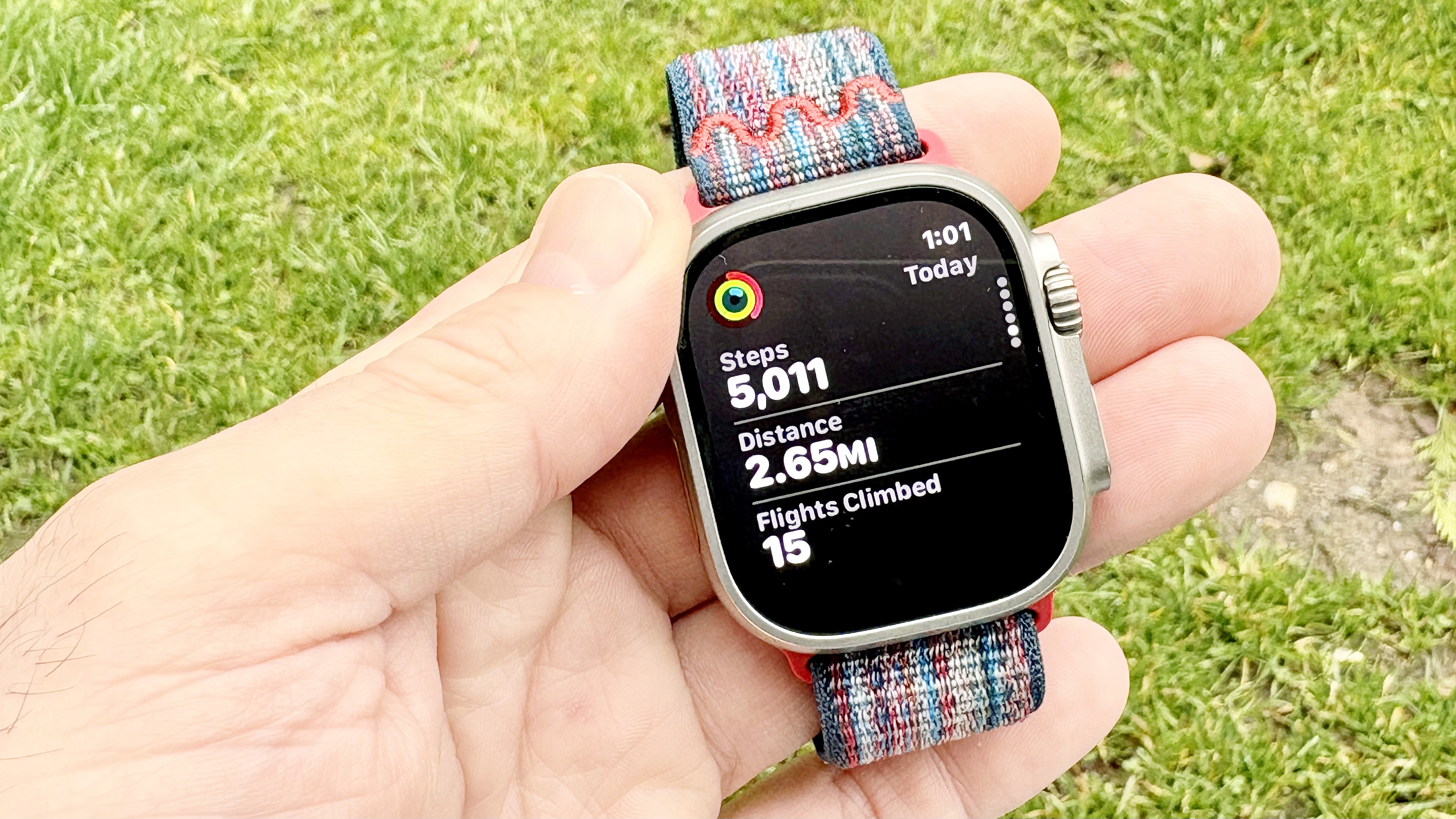 Close-up of the Apple Watch Ultra 3 and Garmin Forerunner 570 in a user's hand with blooming flowers in the background