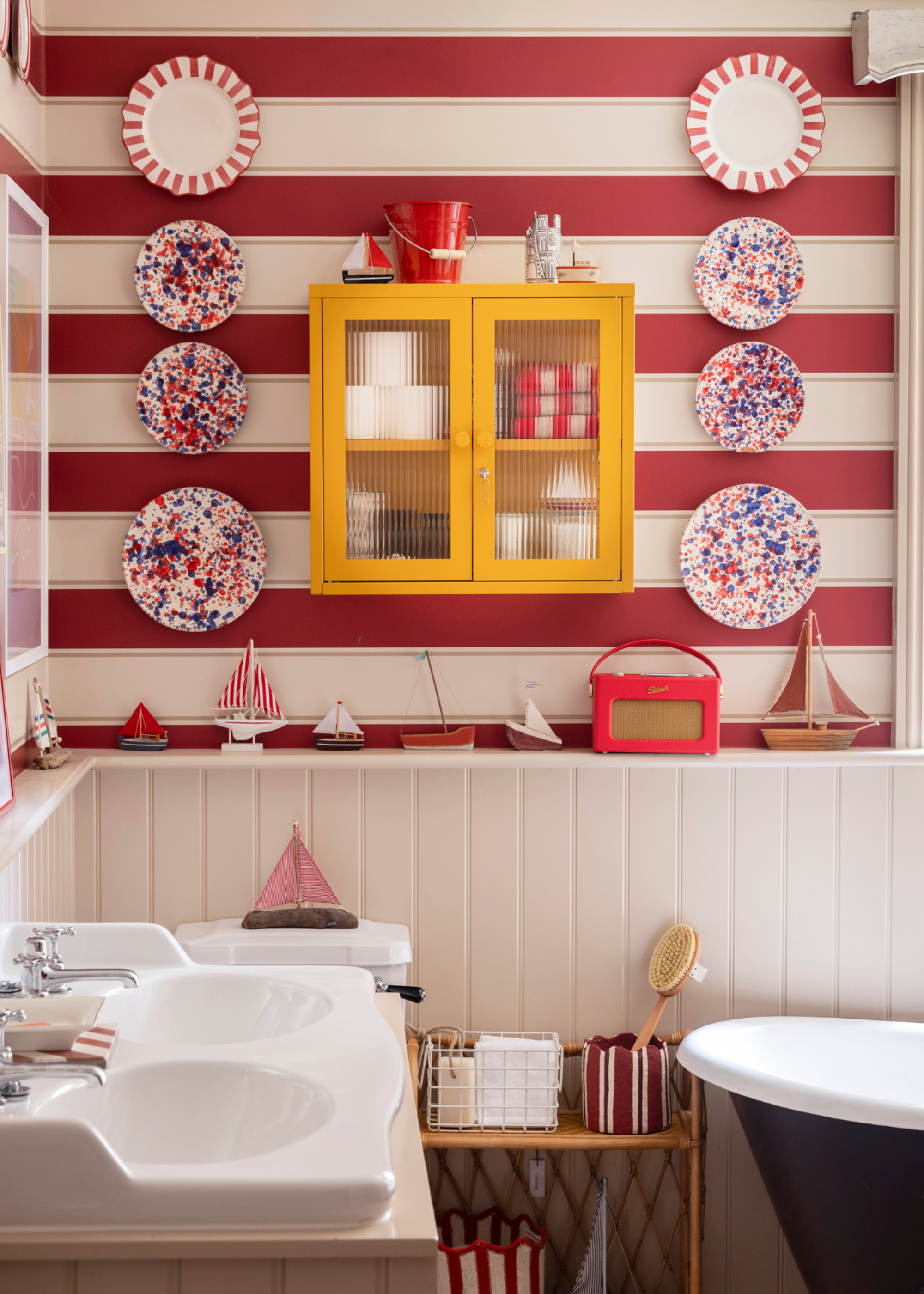 A stripey bathroom with a red theme and a yellow storage cabinet standing out